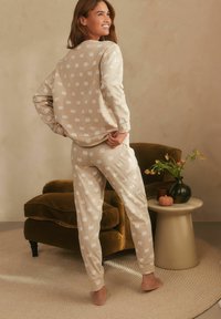 Beige pyjamaset med ett heltäckande vitt pumpa-mönster. Mjuk tyg, avslappnad passform, lång ärm och matchande byxor.