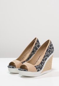 Tacchi wedge con tomaia in finta pelle beige e tessuto a fantasia navy. Suola in gomma bianca con un intersuola intrecciata in stile espadrille.