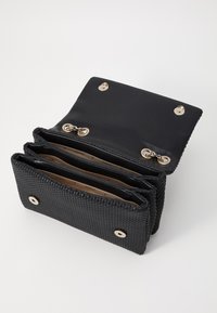 Schwarzes gewobenes Portemonnaie mit strukturiertem Äußeren, goldener Hardware, drei Fächern und einem glatten Innenfutter.