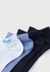 Un sortiment de șosete până la gleznă în albastru deschis, albastru închis, bleumarin și alb. Fiecare prezintă o margine elastică striată și logo-ul „BOSS” în culori contrastante.