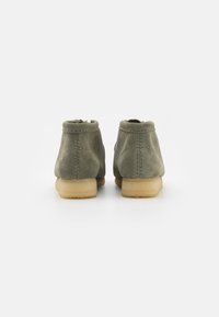 Botas de tornozelo em camurça verde com bicos arredondados, costura mínima e solas de borracha leves, desenhadas para conforto e uso casual.