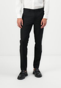 Pantalones negros de corte slim hechos de una tela suave, con un corte clásico, bolsillos laterales y cierre con cremallera. Combinados con mocasines negros.