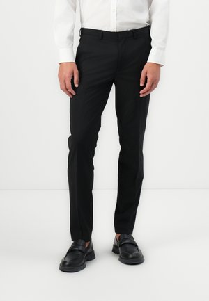 Black slim-fit trousers made from a smooth fabric, featuring a classic cut, side pockets, and a zip fly. Paired with black loafers.