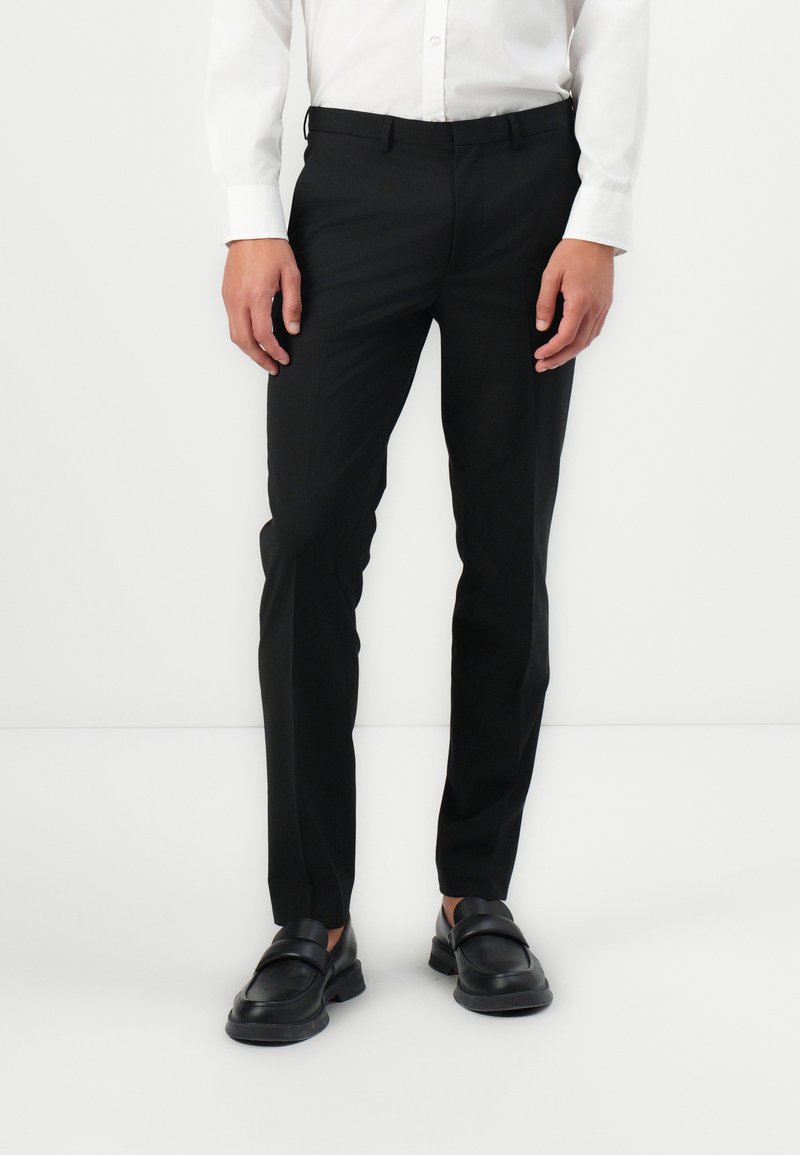 Pantalones negros de corte slim hechos de una tela suave, con un corte clásico, bolsillos laterales y cierre con cremallera. Combinados con mocasines negros.