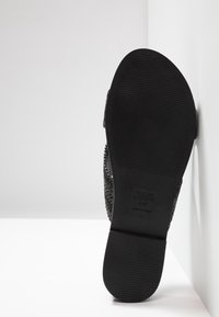 Svart mönstrad sandal med en vävd ovandel och strukturerad gummisula. Har en präglad varumärkesetikett på sulan. Tillverkad i Kina.