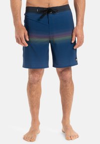 Shorts de bain bleu marine avec une ceinture noire, orn�és de rayures horizontales aux couleurs de l'arc-en-ciel. Tissu léger avec une taille réglable par cordon.