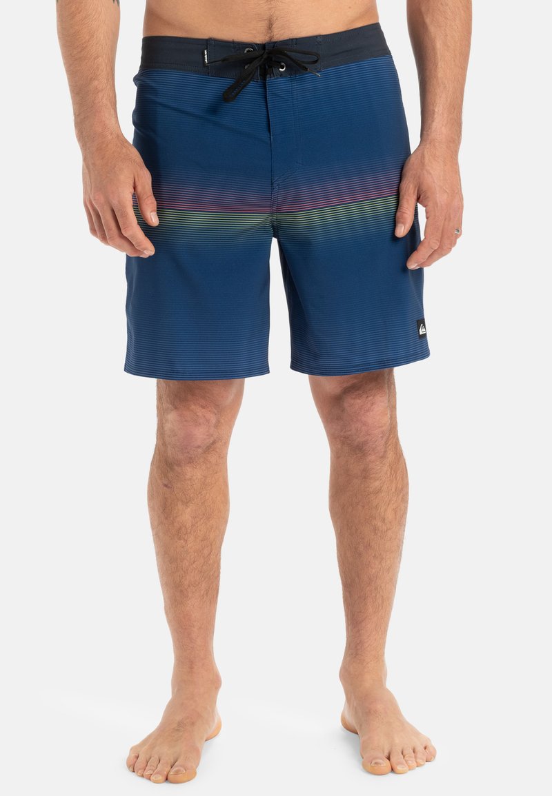 Shorts de bain bleu marine avec une ceinture noire, ornés de rayures horizontales aux couleurs de l'arc-en-ciel. Tissu léger avec une taille réglable par cordon.