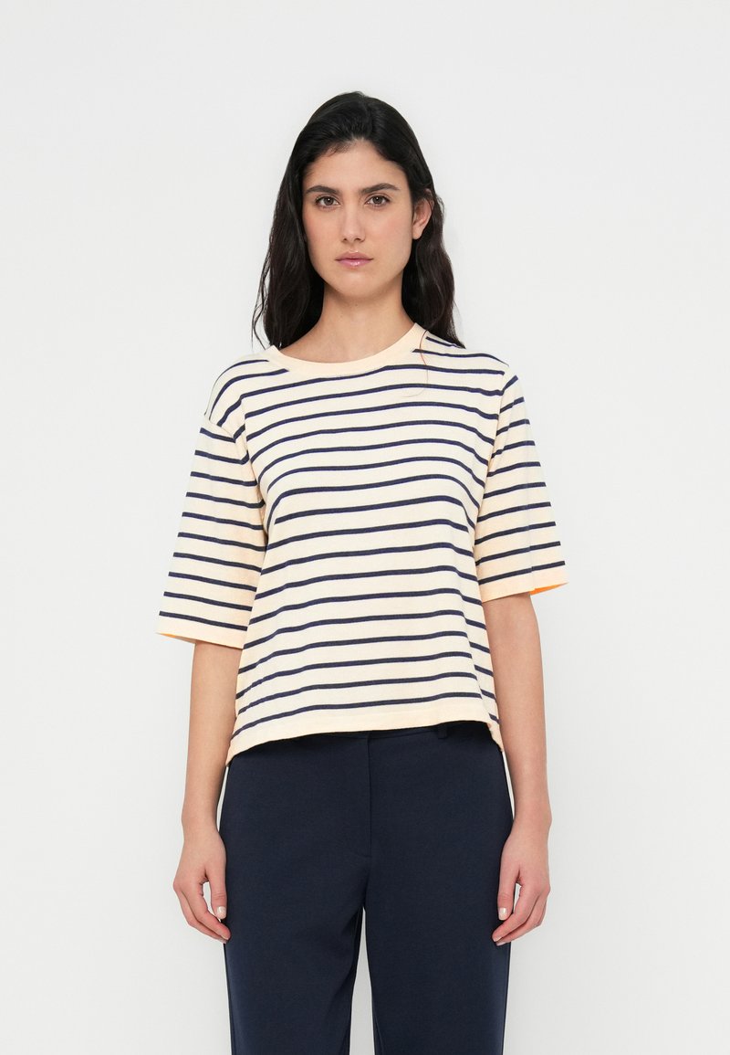 Ριγέ κοντομάνικη μπλούζα σε παστέλ ροδάκινο με μπλε σκούρες ρίγες; στρογγυλή λαιμόκοψη; χαλαρή εφαρμογή; υφή βαμβακερού υλικού με ελαφριά ελαστικότητα.