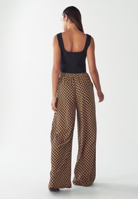 Black sleeveless top paired with loose, brown patterned wide-leg pants featuring a geometric design and elastic waist. Smooth texture.