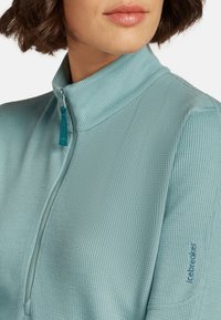 Lichtblauwe zip-kraag top van textuurstof. Heeft een staande kraag en een subtiele merklogo op de mouw.