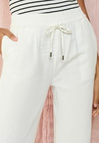 White, loose-fitting pants with an elastic waistband and drawstring. Features side pockets and a textured cotton-like fabric.