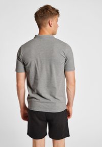 Polo grigio a maniche corte con colletto classico, texture morbida e taglio dritto, indossato con pantaloni corti neri. Vista da dietro.
