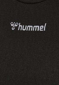 Logo de hummel en blanco con una abeja estilizada encima del texto sobre una tela negra texturizada, probablemente de una prenda de ropa deportiva.