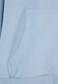 Lysblå sweatshirtstof med en blød tekstur. Har en kængurulomme og ribbet kant. Rene sting langs kanterne.