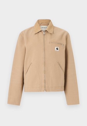 Beige arbeidsjakke med frontglidelås, kordfløyelskrage, sidelommer og glidelåslomme på brystet med Carhartt-logo.