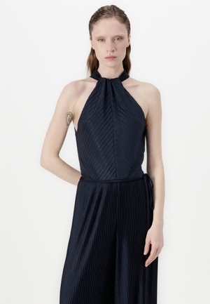 Navy halter jumpsuit with pleated texture, featuring a fitted bodice and flowing wide-leg pants, tied at the waist with a matching fabric belt.