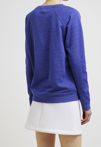 Sudadera azul de tejido texturizado, con cuello redondo y dobladillo acanalado. Combinada con una minifalda blanca de corte acampanado. Diseño sencillo.