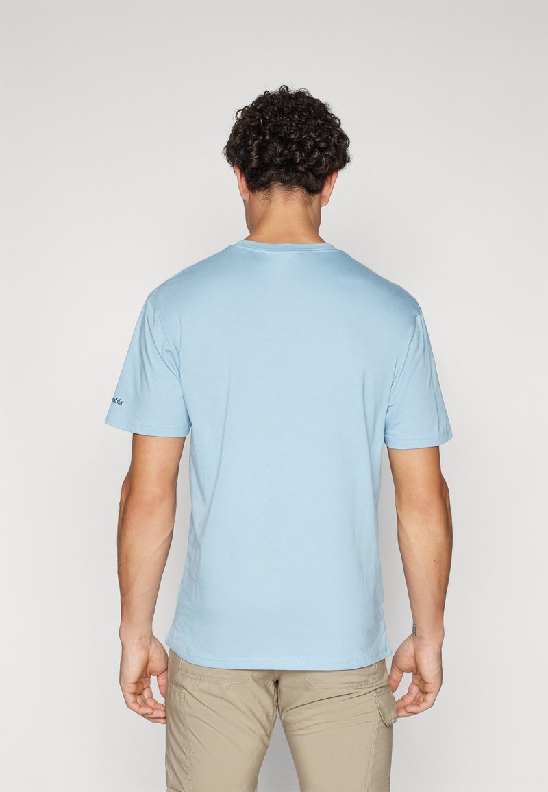 T-shirt bleu clair à manches courtes en tissu lisse. Doté d'un col rond et d'un logo de marque discret sur la manche gauche.