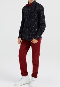 Camisa negra de botones con un patrón de puntos blancos, combinada con pantalones rojo oscuro y zapatillas blancas; incluye una pajarita roja como acento.