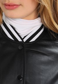 Närbild av en ung kvinna som bär en svart läderjacka med en vit polotröja under, som har en svart- och vitrandig krage.