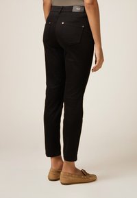 Jeans negros de corte ajustado con una cintura de altura media. Tiene dos bolsillos traseros con herrajes en tono dorado. Llevados con zapatos planos de color marrón claro.