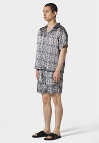 Kurzärmliges Hemd mit Knopfverschluss und Shorts-Set aus gemustertem Stoff in hellgrau und schwarz, mit lockerer Passform und weichem Material.