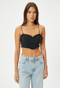 Zwart cropped top met ruches, dunne spaghettibandjes en een sweetheart halslijn, gecombineerd met high-waisted lichtblauwe jeans.