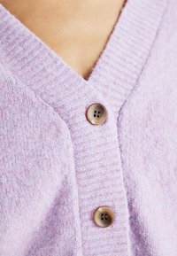 Cardigan viola chiaro con lavorazione a maglia testurizzata, scollatura a V e dettagli con bottoni marroni. Primo piano sui dettagli del tessuto e dei bottoni.