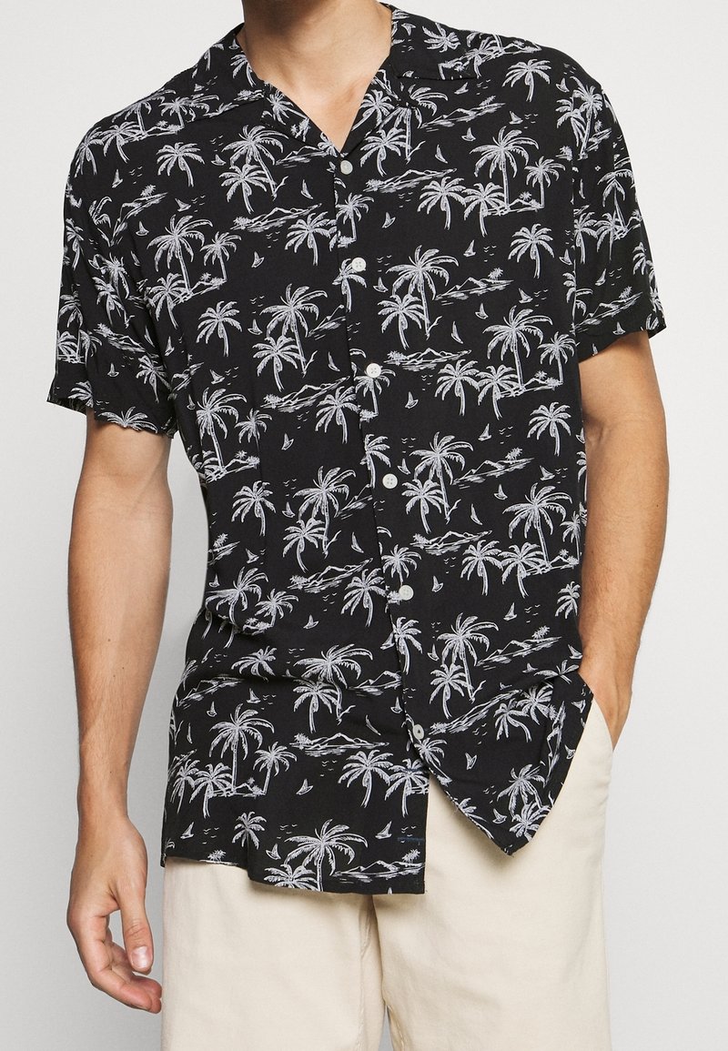 Musta lyhythihainen napillinen paita, jossa valkoinen palmupuukuvio ja purjelaiva. Leikkaus on hieman rento, materiaali kevyt.