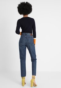 Top de manga larga de canalé en color navy con detalles en naranja, combinado con unos jeans de mezclilla azul de tiro alto y sandalias amarillas de tacón bloque.
