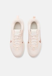Light pink athletic shoes with a textured knit upper, white sole, and bronze Nike swoosh. Features laces and a pull tab at the back.