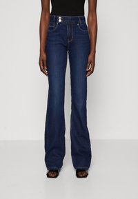 Hochgeschnittene, ausgestellte Jeans aus dunkelblauem Denim, mit zwei Vorderaschen, Knopfverschluss und sichtbaren Nähten entlang der Nähte.