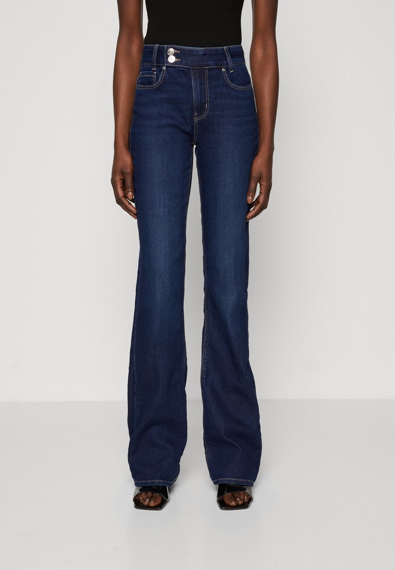 Hochgeschnittene, ausgestellte Jeans aus dunkelblauem Denim, mit zwei Vorderaschen, Knopfverschluss und sichtbaren Nähten entlang der Nähte.