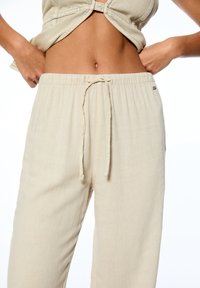 Beige linnen broek met een elastische taille, trekkoordsluiting en een relaxed fit. Soepele textuur en minimale merkdetails aan de zijkant.