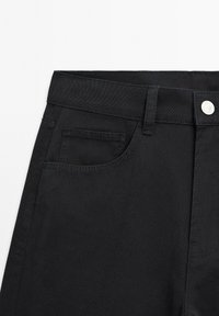Black denim pants with a straight fit, featuring a front pocket, metal button closure, and subtle stitching details on the waistband.