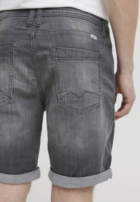 Grå denimshorts har rullekanter, to baklommer med en fjell-lignende sømdesign og en liten merkelapp på midjebåndet.