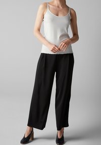 Top de tirantes delgados en gris claro acanalado, combinado con pantalones anchos negros. Botines negros con tacón de madera completan el conjunto.