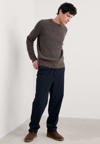 Brązowy sweter z prążkowanego dzianiny, z okrągłym dekoltem; zestawiony z granatowymi spodniami i brązowymi skórzanymi butami. Lekko teksturowany, luźny krój.