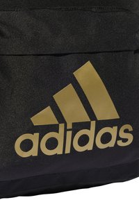 Borsa nera in tessuto con un prominente logo dorato Adidas e tre strisce diagonali. Il materiale è testurizzato, con linee di design pulite.