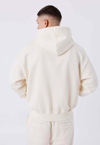 Sudadera color crema con capucha ajustable, puños acanalados y cinturilla. Textura suave, corte oversize y bolsillo canguro en la parte frontal.