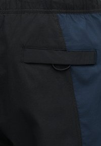 Κοντινή λήψη τσέπης μαύρου και ναυτικού σορτς με καπάκι και μαύρη ελαστική μέση.