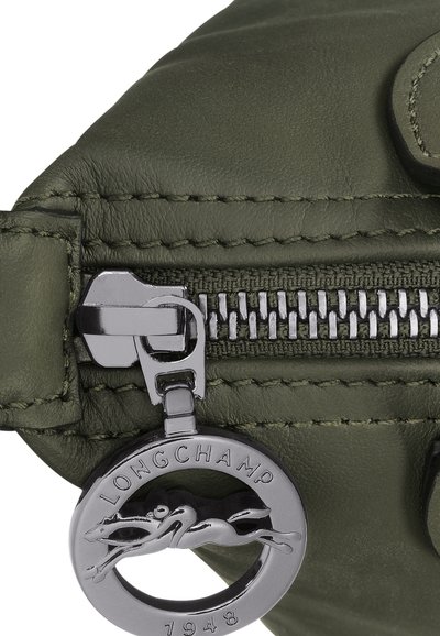 Olivengrüne Lederhandtasche mit silbernem Reißverschluss und runder Anhänger mit einem Greyhound-Logo, genähten Kanten und texturierter Oberfläche.