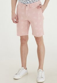 Pantaloni scurți de culoare roz deschis, din bumbac, cu un model de palmieri, buzunare laterale și închidere cu nasturi. Purtați cu adidași albi.