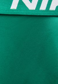 Κοντινό πλάνο υφάσματος μπλε-πράσινου χρώματος με ραβδωτή υφή, με λευκή και πράσινη πλεκτή άκρη και μερικώς ορατό κείμενο.