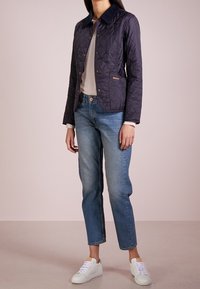 Gequilted marineblauwe jas met een kraag, drukknoopsluiting, zijzakken en een logo-accent. Draag het met lichtblauwe jeans en witte sneakers.