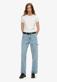 Camisa de algodón blanca combinada con jeans de mezclilla azul claro de corte recto, con cierre de botón y cinturón de cuero negro. Zapatos negros.