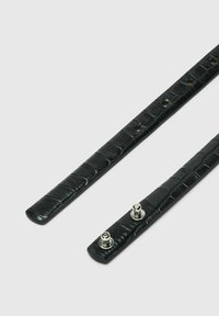 Lanières en cuir noir avec une texture crocodile, équipées de ferrures en argent et de multiples trous de réglage pour un ajustement parfait.