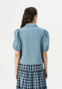 Lichtblauwe spijkerjack met opgezette mouwen, een klassieke kraag en een cropped model, gecombineerd met een marineblauwe geruite rok.