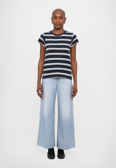 Stribet navy og hvid t-shirt med korte ærmer, parret med højtaljede, vidde lyseblå denim jeans og sorte sko.