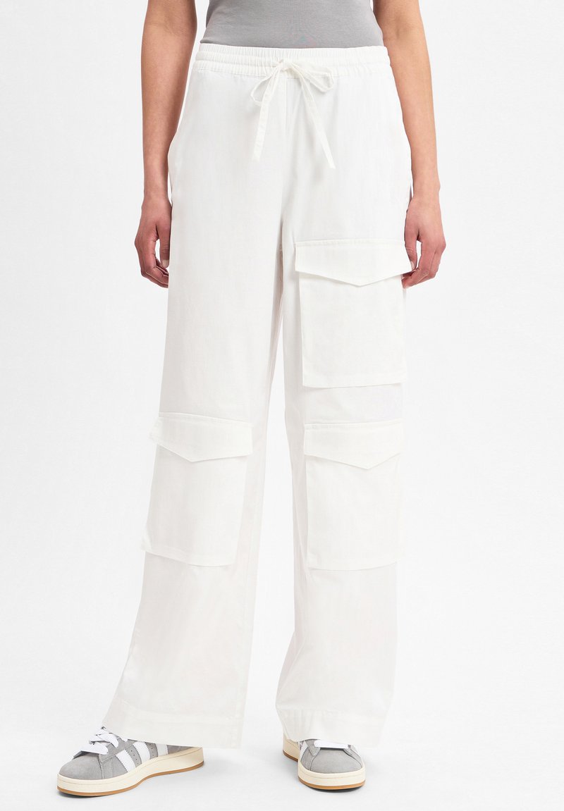 Witte cargobroek met een elastische tailleband en trekkoord, voorzien van meerdere grote zakken. Gekoppeld aan grijze sneakers.